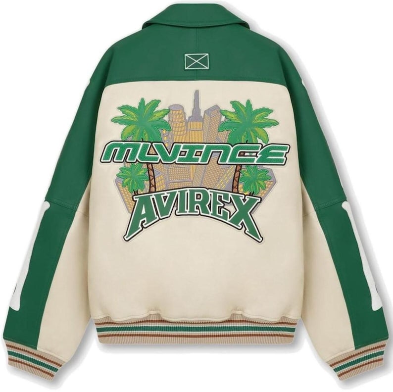 May include: Green and cream-colored bomber jacket with a button-down collar. The back features an embroidered design with palm trees, a cityscape, and the text "MLVINCE AVIREX" in green. The jacket has green sleeves and a striped hem.