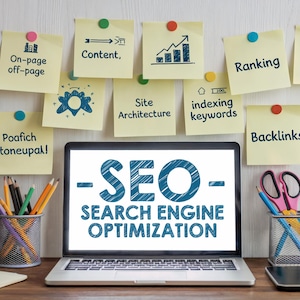 Könnte beinhalten: Ein Laptop zeigt "SEO - SEARCH ENGINE OPTIMIZATION" in blauer Schrift. Gelbe Haftnotizen mit SEO-Begriffen wie "Inhalte" und "Backlinks" sind darüber gepinnt. Bleistifte und Scheren befinden sich in Metallbehältern.