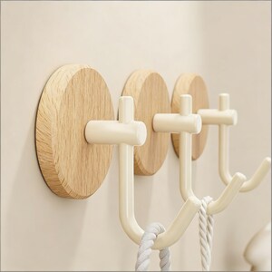 May include: Three wall-mounted coat hooks. Each hook has a round, light-coloured wooden base with a white metal hook. The hooks are designed for hanging items such as coats or bags. The design is minimalist and modern.