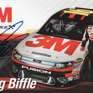 May include: A promotional image featuring a race car with the 3M logo and the name "Greg Biffle." The car is white, red, and black, with the number 16. A driver in a racing suit stands next to the car, holding a helmet.