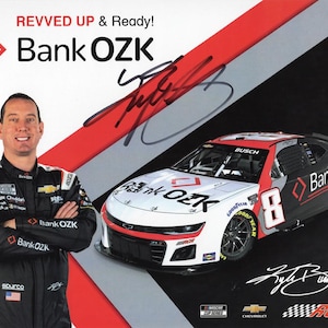 Op de afbeelding: Een promotieafbeelding met een raceauto en een coureur. De auto is wit, zwart en rood, met "Bank OZK" branding. De coureur, in een zwart racepak, staat met gekruiste armen. De afbeelding bevat de tekst "REVVED UP & Ready!"