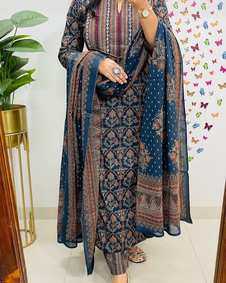Może przedstawiać: Ciemnoniebieski indyjski zestaw salwar kameez z pasującą dupattą. Str&oacute;j ma skomplikowane wzory kwiatowe i geometryczne w odcieniach czerwieni, brązu i bieli. Top z długim rękawem ma dekolt w kształcie dziurki od klucza.