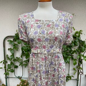 May include: A white maxi dress with a floral print in shades of pink, purple, and brown. The dress has a square neckline, short sleeves, and a button-up front.