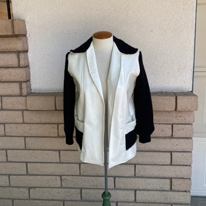 May include: A white faux leather jacket with black knit sleeves. The jacket has a zipper closure and two pockets.