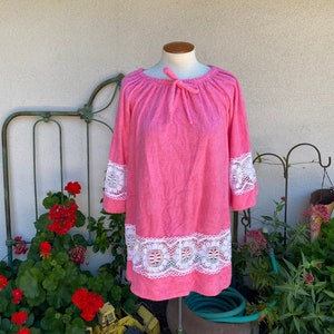 May include: A pink terry cloth robe with white lace trim around the neckline, sleeves, and hem. The robe has a tie at the neckline.
