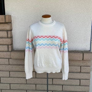 May include: A white sweater with a colorful chevron pattern. The pattern is made up of pink, blue, green, and yellow stripes.