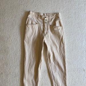 May include: A pair of light beige, high-waisted jeans with a button fly and unique pocket detailing.