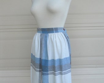 May include: A white skirt with a blue and gray plaid pattern. The skirt has a button closure on the side and a gathered waistband.