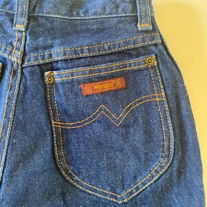 May include: A pair of dark blue denim jeans with a back pocket featuring a brown leather Wrangler label.