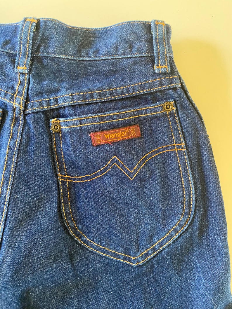 May include: A pair of dark blue denim jeans with a back pocket featuring a brown leather Wrangler label.