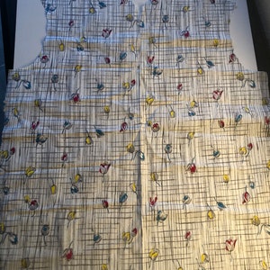 May include: A white fabric with a grid pattern and small floral designs in red, blue, and yellow.