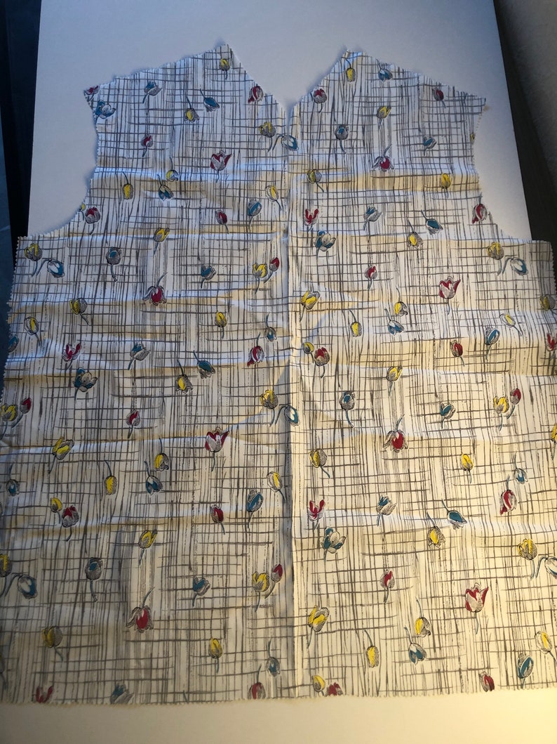 May include: A white fabric with a grid pattern and small floral designs in red, blue, and yellow.