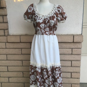 May include: A long white maxi dress with brown floral print and lace trim. The dress has a fitted bodice and a flowing skirt.