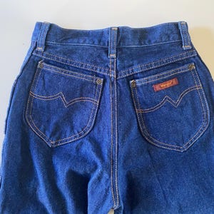 May include: A pair of dark blue denim jeans with a brown leather patch that says "Wrangler" on the back right pocket.