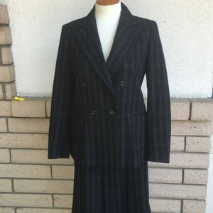 May include: A black and green plaid skirt suit with a double-breasted blazer. The blazer has two buttons and a pocket on the left side. The skirt is pleated and falls to the knees.