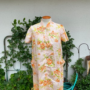 May include: A pink and orange floral print robe with a zipper closure and short sleeves. The robe has two pockets on the front.
