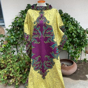May include: A yellow and purple maxi dress with a floral pattern. The dress has a high neck and long sleeves. The fabric is soft and flowy.