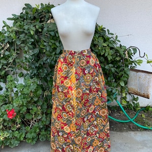 May include: A long, quilted skirt with a floral print in shades of red, orange, yellow, and green. The skirt is gathered at the waist and has a full, flowing silhouette.