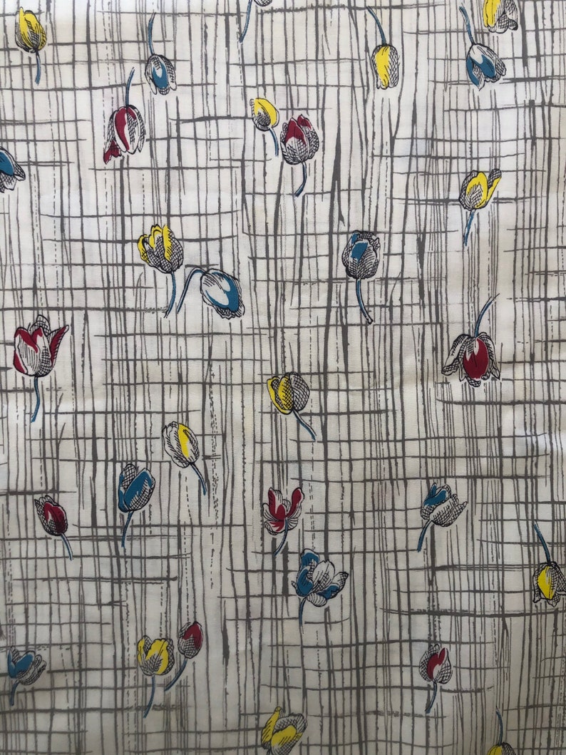 May include: A white fabric with a repeating pattern of stylized tulips in shades of red, yellow, blue, and gray. The tulips are arranged on a grid of thin black lines.
