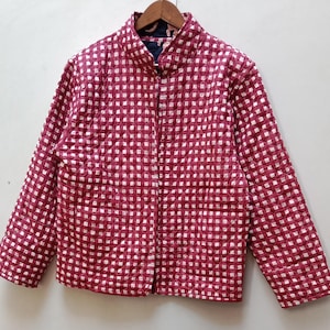 以下が含まれることがあります： 赤と白のチェック柄のキルティングジャケット。 ジャケットはスタンドカラー、長袖、ボタン留めのフロントが付いています。 ジャケットは木製のハンガーに掛けられています。