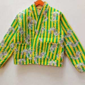 Puede incluir: Chaqueta acolchada con un vibrante estampado de rayas verticales amarillas y verdes. La chaqueta presenta un cuello en V, dos bolsillos y un diseño repetido de tigres blancos. La chaqueta mide aproximadamente 61 cm de largo.
