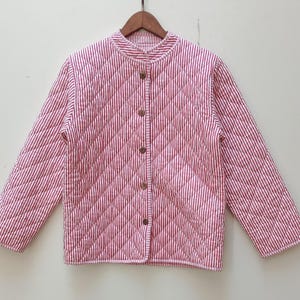 May include: A quilted jacket with a red and white striped pattern. The jacket has a round collar, long sleeves, and wooden buttons down the front. The fabric is stitched in a diamond pattern.
