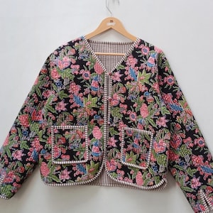 Könnte beinhalten: Gesteppte Jacke mit floralem Muster auf schwarzem Grund, mit rosa, grünen und blauen Blumen. Die Jacke hat zwei Vordertaschen und ein gestreiftes Futter. Auf einem Holzbügel aufgehängt.