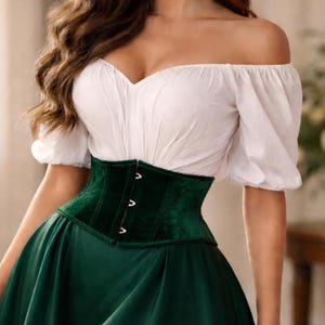 Peut inclure: Un chemisier blanc à épaules dénudées et manches courtes, associé à un corset en velours vert foncé et une jupe verte assortie. Le corset comporte trois fermoirs argentés. L'ensemble est un mélange de styles classiques et modernes.