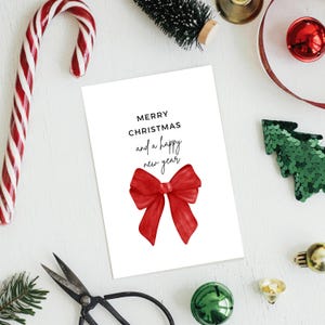 Puede incluir: Una tarjeta de Navidad blanca con el mensaje "MERRY CHRISTMAS and a happy new year" y una ilustración de un lazo rojo. La tarjeta está rodeada de decoraciones navideñas, incluyendo un bastón de caramelo, adornos y un árbol de Navidad con lentejuelas.