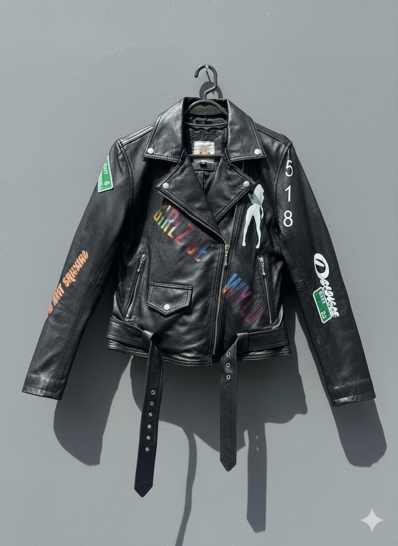 May include: Black leather jacket with a classic biker style, featuring a notched collar, asymmetrical zipper, and a belted waist. The jacket is adorned with colorful graffiti-style graphics and the number 518.