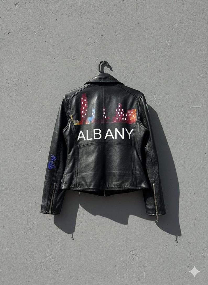 May include: Black leather jacket with a colorful Albany skyline design on the back. The jacket has a classic biker style with a zipper closure and a small graphic on the sleeve. The word "ALBANY" is printed in white.