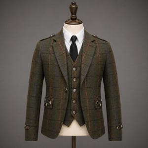 Könnte beinhalten: Ein dreiteiliger Anzug bestehend aus einem dunkelolivgrünen Blazer und einer Weste mit braun-blauem Fensterkaro-Muster. Der Blazer hat ein steigendes Revers, Pattentaschen mit Zierknöpfen und Schulterklappen. Dazu ein weißes Hemd und eine schwarze Krawatte.