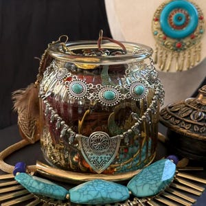 May include: A glass jar filled with jewellery, including necklaces, earrings, and bracelets. The jewellery features turquoise and silver accents. A feather and a gold-toned necklace are also visible.