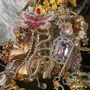Può includere: Un assortimento di gioielli ornati, tra cui collane, bracciali e ciondoli. La collezione presenta toni oro e argento, con accenti di pietre preziose rosa, rosse e verdi. I disegni di farfalle e fiori sono prominenti, creando un'estetica lussuosa e dettagliata.
