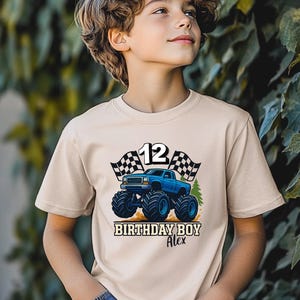 May include: A beige t-shirt featuring a blue monster truck design with the number 12, checkered flags, and the text "BIRTHDAY BOY Alex". The graphic is centered on the front of the shirt.