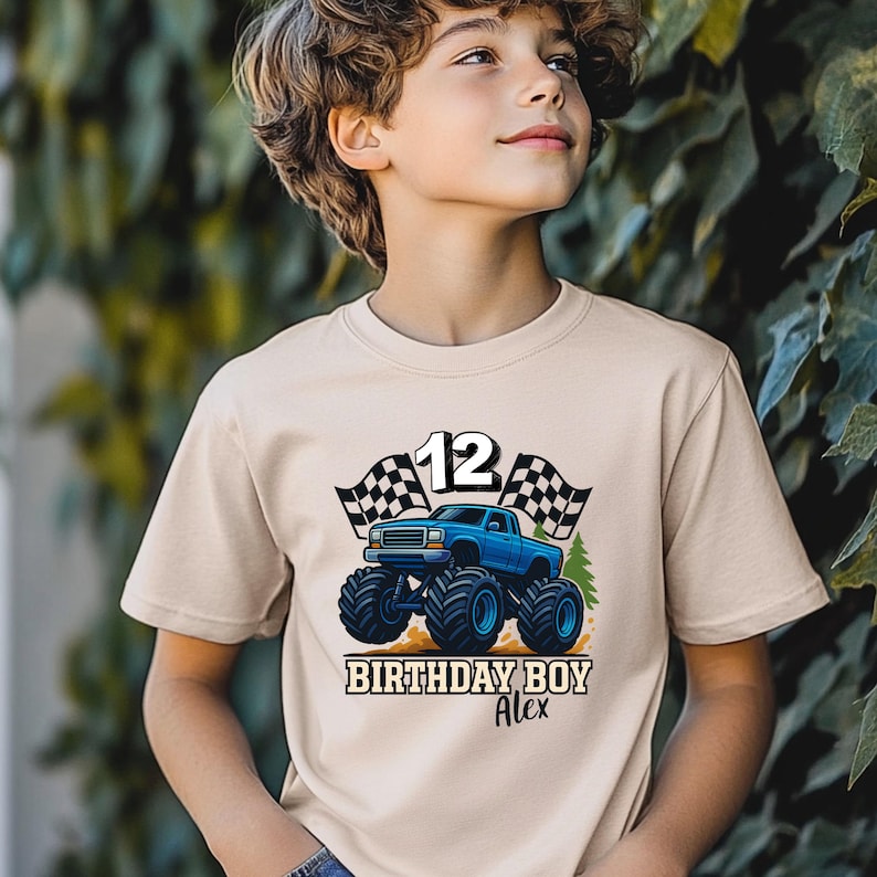 May include: A beige t-shirt featuring a blue monster truck design with the number 12, checkered flags, and the text "BIRTHDAY BOY Alex". The graphic is centered on the front of the shirt.
