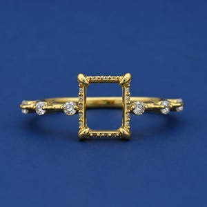 Puede incluir: Un anillo de oro con un engaste central en forma de marco rectangular adornado con pequeñas piedras claras. La banda está decorada con piedras redondas claras adicionales colocadas a intervalos a lo largo de los lados.