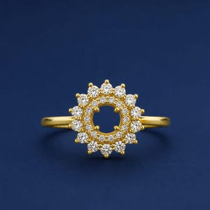 Puede incluir: Un anillo de oro con una pieza central circular con diseño de rayos de sol. El centro está abierto, rodeado por dos filas concéntricas de pequeñas piedras claras de corte redondo engastadas en oro, creando un aspecto floral brillante y detallado.