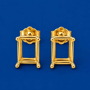 Puede incluir: Un par de monturas para pendientes de botón en tono dorado con un diseño rectangular de cuatro garras. Cada montura incluye un perno y un cierre de mariposa a juego, con un acabado metálico pulido y una estructura definida.