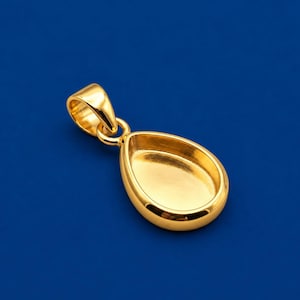 Peut inclure: Un pendentif en forme de goutte d'eau de couleur dorée polie, doté d'un centre lisse et évidé ainsi qu'une bélière arrondie sur le dessus. La surface métallique présente une finition brillante et réfléchissante au design simple et épuré.