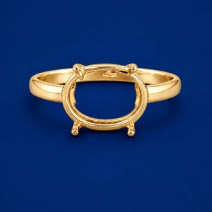 May include: A polished yellow gold ring setting featuring an oval-shaped basket with four prongs designed to hold a gemstone. The band is smooth and rounded, showcasing a classic metal finish without any stones or additional decorative elements.