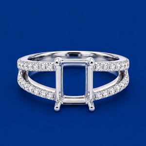 Può includere: Una montatura per anello color argento con un design a fascia divisa, decorata con piccole pietre trasparenti a taglio rotondo. Il centro dell'anello presenta un supporto rettangolare a quattro griffe per una gemma.