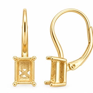 May include: A pair of gold leverback earring settings featuring a rectangular prong setting designed to hold a gemstone. The metal has a polished finish, and the earring components include a hinged closure mechanism for secure attachment.