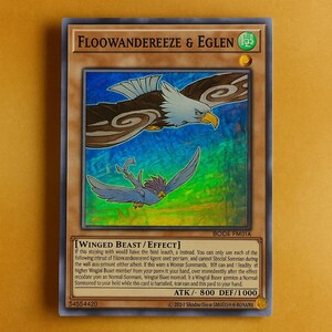 May include: A trading card featuring two stylized birds, one eagle-like and the other smaller, against a colorful background. The card has text in English, including the name "FLOOWANDEREEZE & EGLEN" and game-related details.