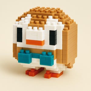 May include: A 3D owl figure constructed from small, colorful building blocks. The owl features a tan body, white face, black eyes, orange beak, and blue accents. The toy is designed to resemble a pixelated or blocky aesthetic.