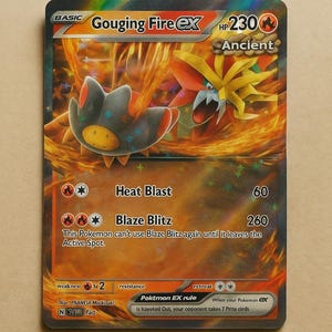 May include: A Gouging Fire ex Pokémon card with a fiery background. The card features a creature with orange and black coloring, with the text "Heat Blast" and "Blaze Blitz" detailing attack moves. The card has a HP of 230.