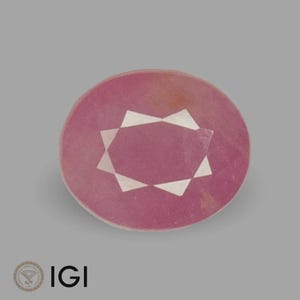 May include: A round, pink gemstone with a starburst design in the center. The gemstone has a polished surface and is set against a gray background. The IGI logo is in the lower left corner.