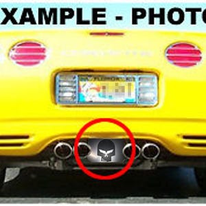 May include: Rear view of a bright yellow sports car with the text "EXAMPLE - PHOTO" at the top. The car has four exhaust pipes and a license plate. A black and white skull emblem is highlighted.