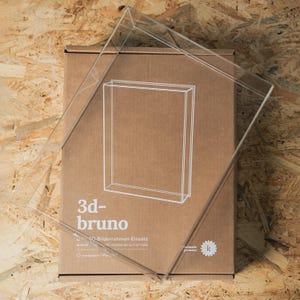 Könnte beinhalten: Ein klarer Acryl-Bilderrahmen liegt auf einem Karton. Auf dem Karton befindet sich eine weiße Umrisszeichnung eines Rahmens und der Text "3d-bruno". Der Rahmen ist transparent und scheint zur Aufnahme eines dreidimensionalen Objekts bestimmt zu sein.