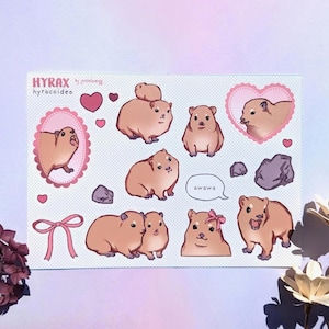 Könnte beinhalten: Ein Stickerbogen mit Illustrationen von Klippschliefern in verschiedenen Posen. Die Aufkleber sind in Braun- und Rosatönen gehalten, mit Herzen, einer Schleife und dem Text "awawa". Das Blatt enthält den Text "HYRAX hyracoidea".